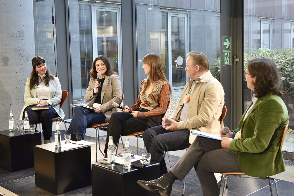 5 Personen sitzen auf einer Bühne und unterhalten sich